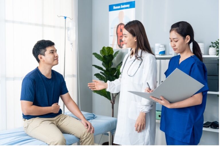 A female specialist doctor and nurse assist a male patient who suffers from rectal prolapse. Explaining to the patient the causes and symptoms of rectal prolapse